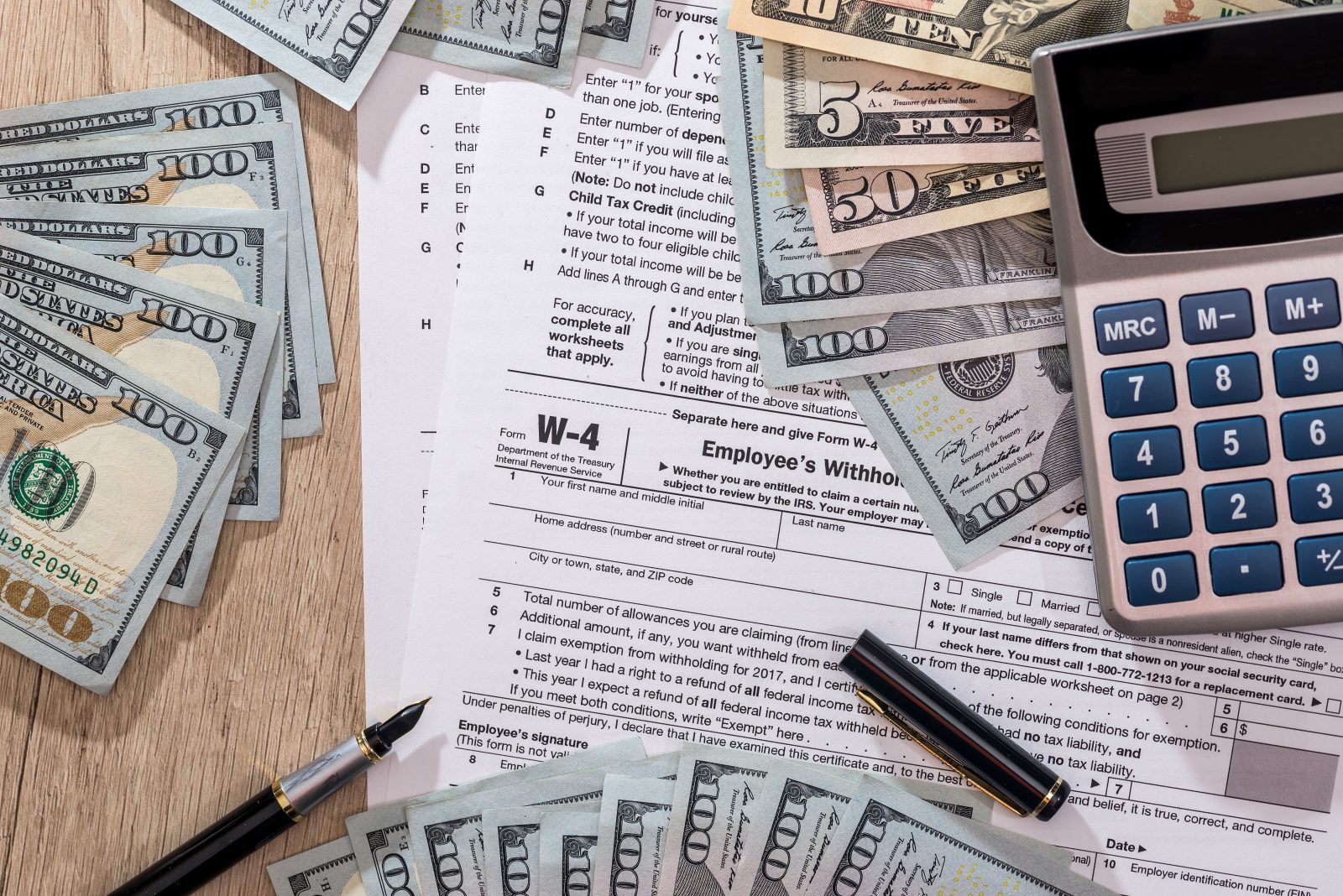 w4 tax form with money, pen and calculator on desk.